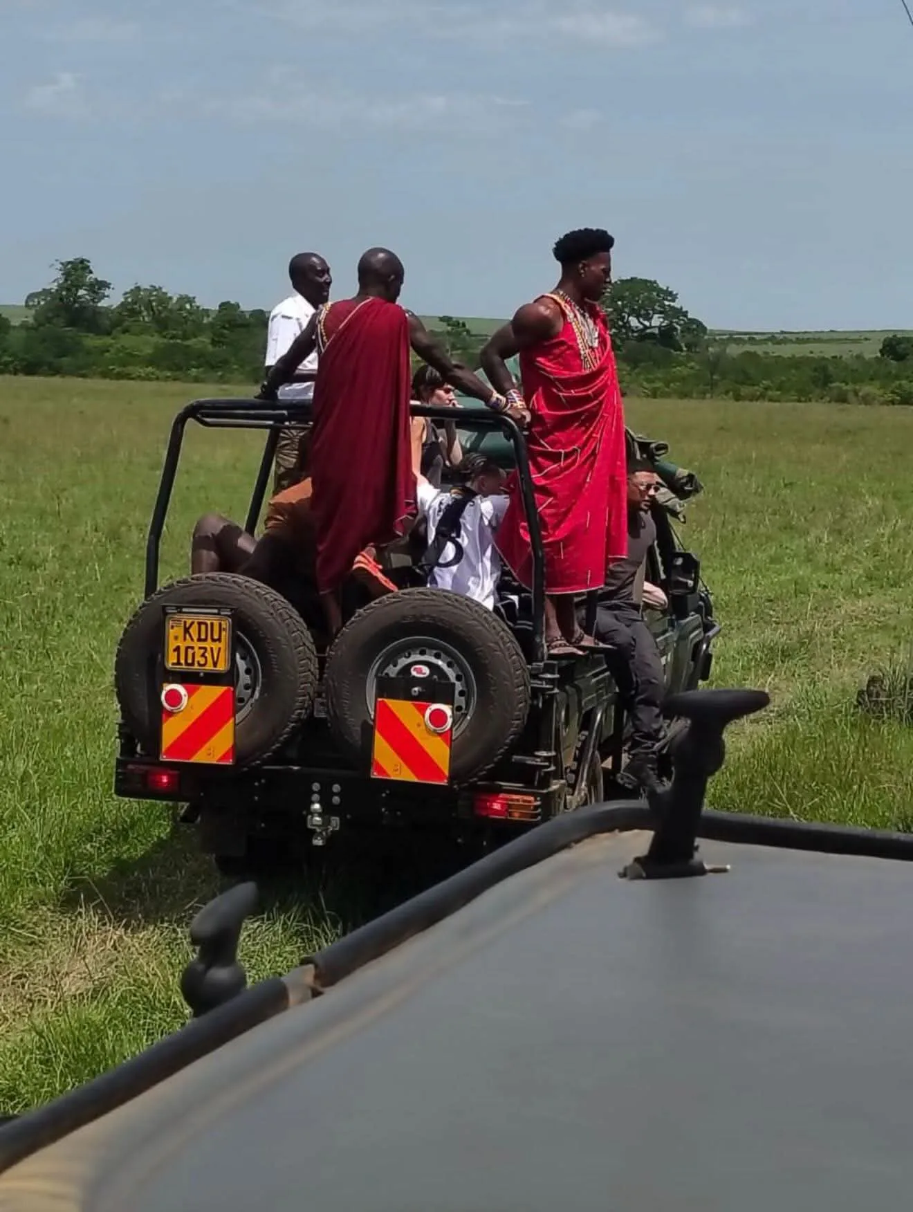 Safari guests traveling with Maasai hosts in an open vehicle
